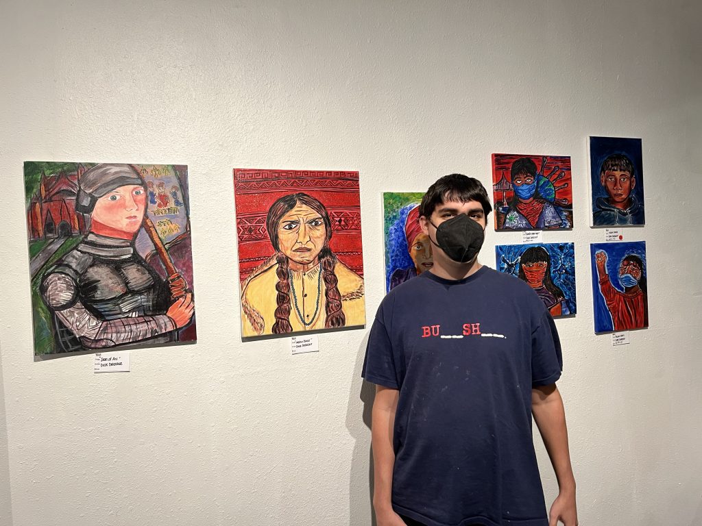 Dusk Delacour at his 2022 exhibition, standing before his colorful portraits